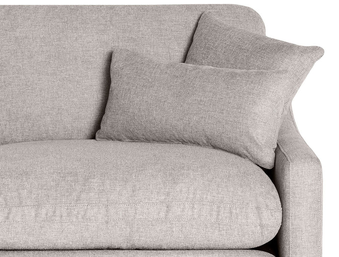 Close-up of a gray fabric sofa with a soft, textured finish. A matching pillow rests on the seat, and another is propped against the armrest, creating a cozy, inviting appearance.