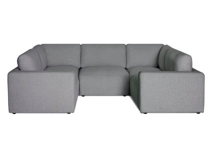 Modern living room with a large, light gray sectional sofa, a blue patterned accent wall, and a standing floor lamp. A dark blue and white rug lies on a dark wood floor. A window lets in natural light.