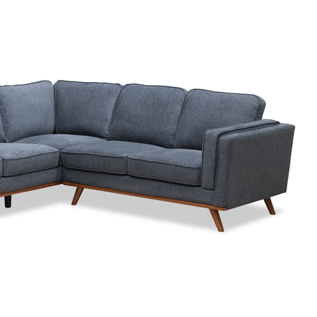 The Maddox RSF is a stylish L-shaped sofa with dark gray upholstery and wooden legs, embodying mid-century modern design. Its plush cushions and clean lines make it ideal for a contemporary living room.
