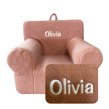 The My Cloud Kidz Chair is a plush pink sherpa armchair for children with Olivia embroidered on the backrest. It has a textured fleece-like look and includes an inset showing the embroidery detail, plus a top loop handle for easy carrying.