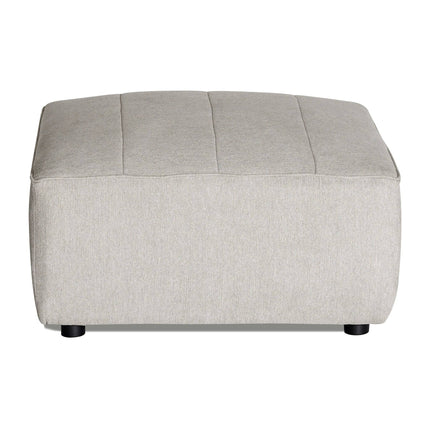 The Millenium Ottoman is a light gray, rectangular piece with a smooth fabric surface, subtle horizontal seams, and small black legs. It complements any modular sofa with its modern luxury style.