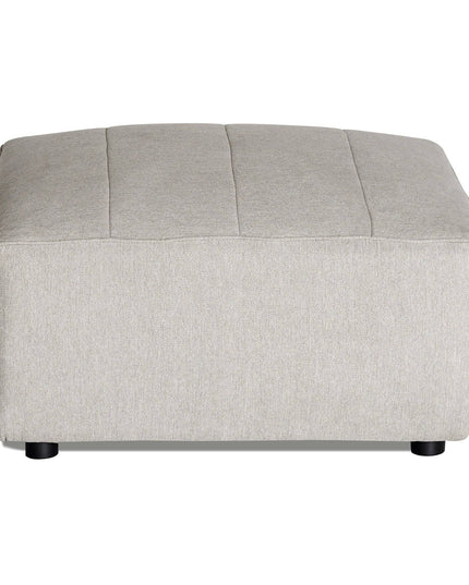 The Millenium Ottoman is a light gray, rectangular piece with a smooth fabric surface, subtle horizontal seams, and small black legs. It complements any modular sofa with its modern luxury style.