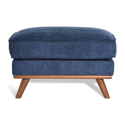 The Maddox Ottoman features textured blue upholstery and a rectangular cushion. Its mid-century design includes a wooden frame with four angled legs in a natural finish, making it an elegant addition to any living space.