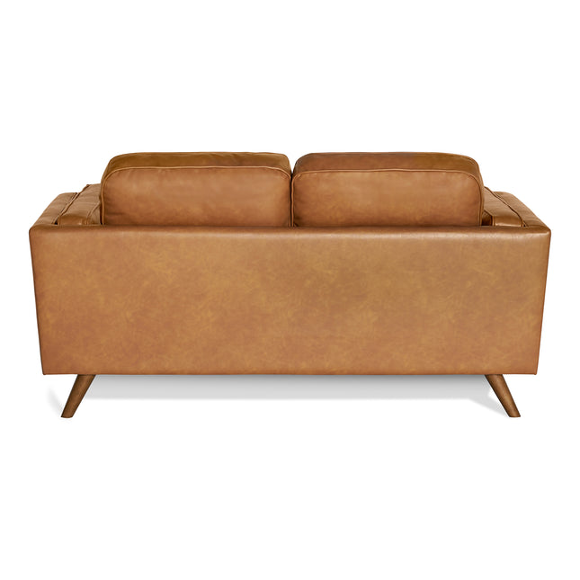 Back view of the Maddox Loveseat showcasing its mid-century modern design with tan leather upholstery. It features two large cushions and outward-angled wooden legs, set against a plain white background, highlighting its durable construction and retro charm.