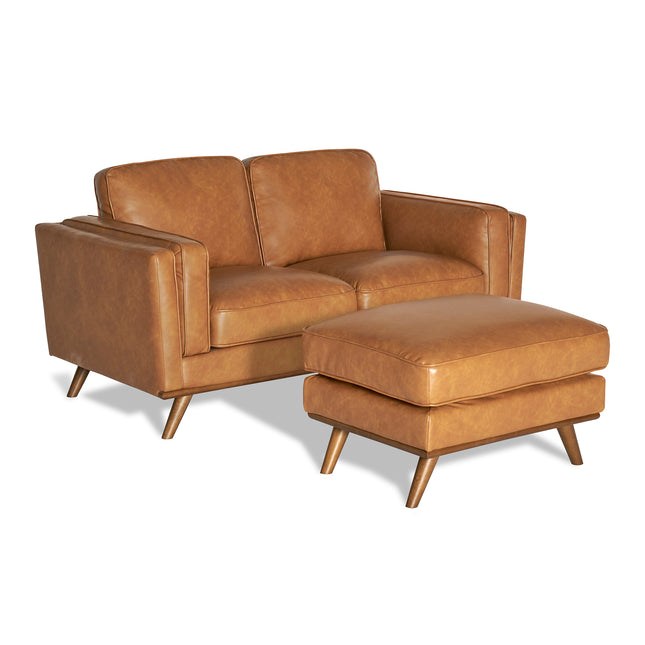 The Maddox Loveseat, in brown leather with tufted cushions, is paired with a matching ottoman. Both pieces feature angled wooden legs and a mid-century modern design, crafted for durability, standing out against the plain white background.