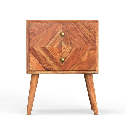 The MCM Bedside Table, crafted from solid mango wood, features two drawers with natural wood grain and brass knobs. It stands on four angled legs with a simple, modern design and a warm, rustic finish.