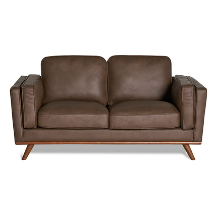 The Maddox Loveseat is a brown leather piece featuring a mid-century modern design, with two seat and back cushions, angular armrests, and four wooden legs for contemporary aesthetics and durability.