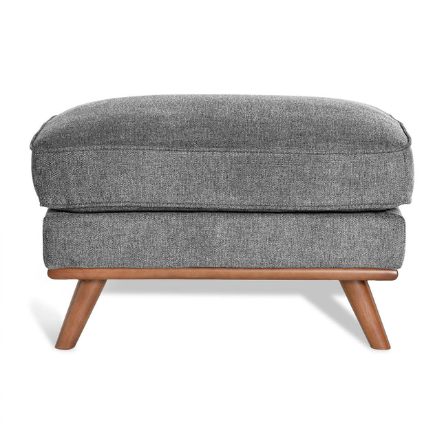 The Maddox Ottoman has a gray upholstered rectangular cushion with subtly textured fabric, supported by four angled wooden legs, adding mid-century charm to any living space.