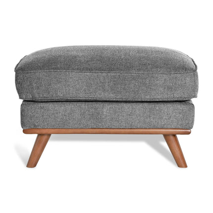 The Maddox Ottoman has a gray upholstered rectangular cushion with subtly textured fabric, supported by four angled wooden legs, adding mid-century charm to any living space.