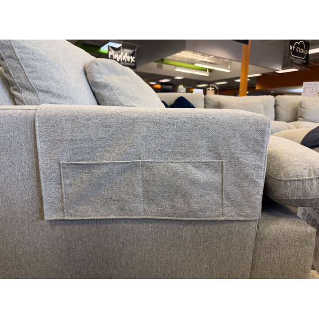 In a brightly lit showroom, the My Cloud Arm Covers in light gray showcase a sewn-on pocket on the couch armrest. Other furniture and store signage enhance the appeal of this washable, practical addition.