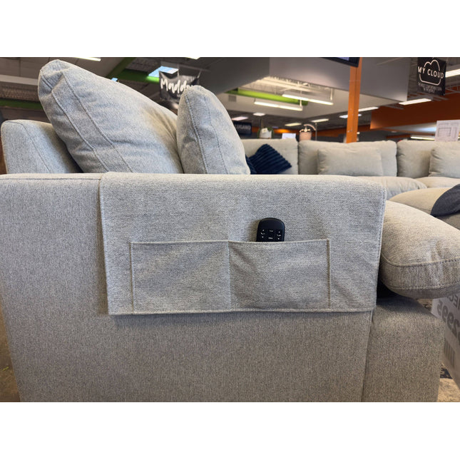 A light gray sofa, featuring My Cloud Arm Covers and a fabric pocket ideal for a remote control, is displayed in a furniture store along with other couches.