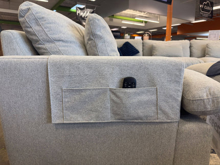 A light gray sofa, featuring My Cloud Arm Covers and a fabric pocket ideal for a remote control, is displayed in a furniture store along with other couches.