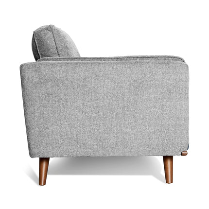 The Maddox Chair, featuring a modern gray fabric with a boxy design inspired by mid-century modern style, has plush cushions, wooden legs, and a slightly reclined backrest. It is showcased against a plain white background.