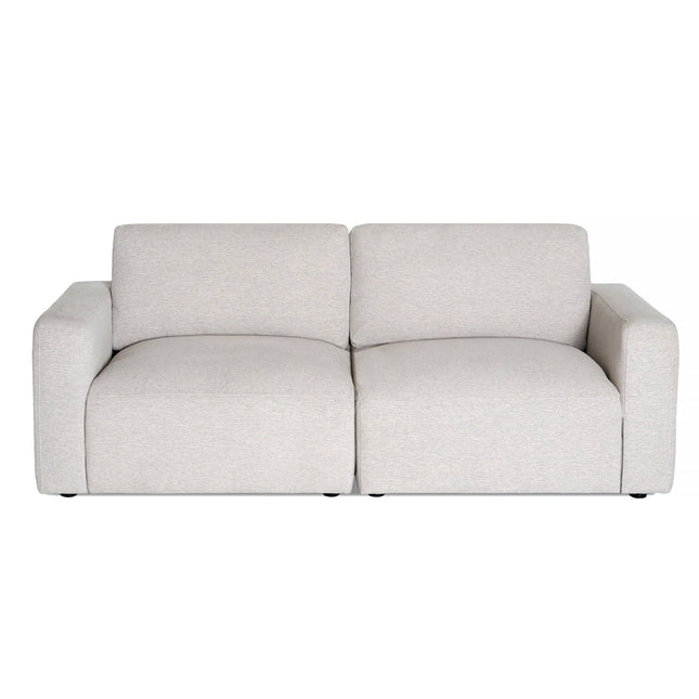 The Lugano sectional sofa features a contemporary beige design with plush cushions, wide armrests, and a low backrest. Its soft, textured fabric exudes Italian luxury, ideal for modern living spaces against a plain white background.