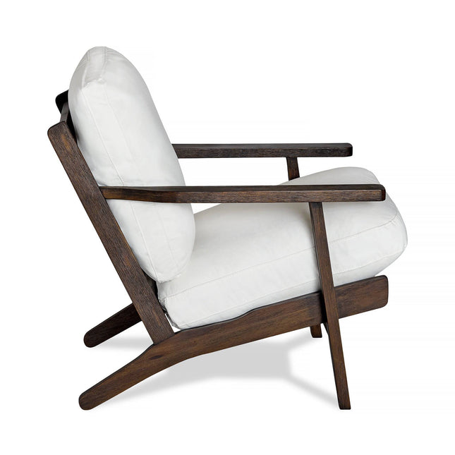 The Peyton Chair features a side view with a dark wooden frame and white cushions. Its mid-century modern design has sleek, angled legs that seamlessly blend minimalist aesthetics with comfort.