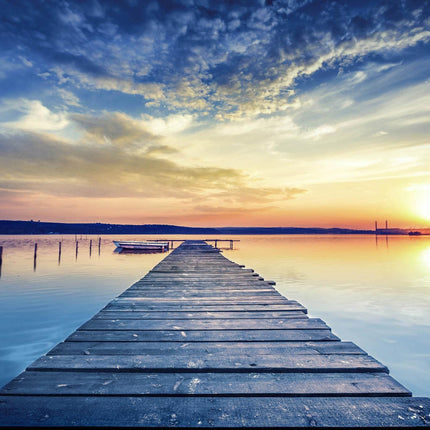 The Sunset Dock extends over a tranquil lake, reflecting the sunsets vibrant hues like museum-quality art. The sky merges deep blues with warm oranges and scattered clouds, while a small boat moored beside the dock adds to the serene ambiance.