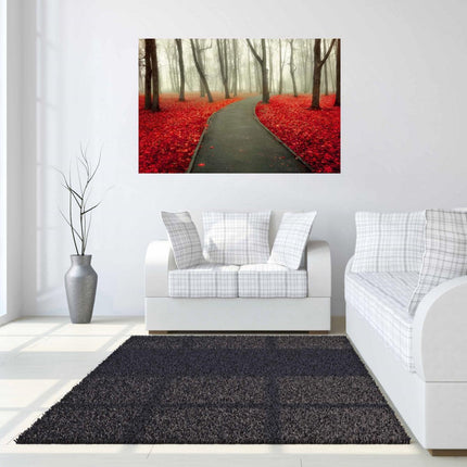 A modern living room boasts white sofas, a dark rug, and Red Autumn, a large picture depicting a misty forest path with vibrant red leaves, akin to museum-quality artwork. The space includes a tall plant in a gray vase and expansive windows that fill the room with natural light.