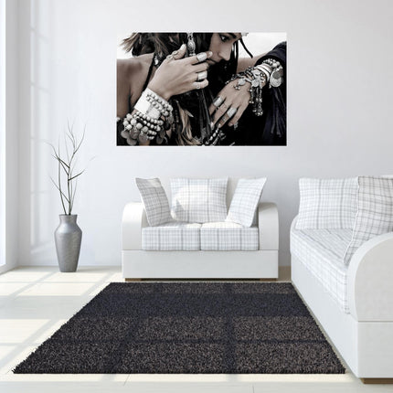 Modern living room featuring a white sofa and loveseat with plaid cushions. A large, museum-quality Boho Jewels photograph hangs above the loveseat. Nearby, a tall plant in a gray vase stands by the window, while a dark rug highlights the light floor.