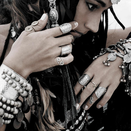 A woman wearing Boho Jewels, featuring intricate silver rings, bracelets, and necklaces, exudes a museum-quality bohemian style. With her hands near her face as she looks down, the detailed designs of her accessories craft a lasting impression.