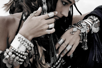 A woman wearing Boho Jewels, featuring intricate silver rings, bracelets, and necklaces, exudes a museum-quality bohemian style. With her hands near her face as she looks down, the detailed designs of her accessories craft a lasting impression.