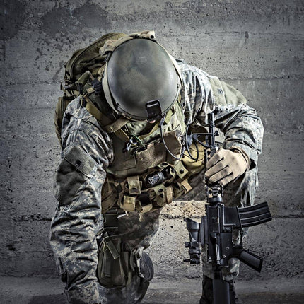 The Kneeling Soldier depicts a camouflaged soldier with one knee on the ground, holding a rifle vertically. Dressed in tactical gear and helmet, they are set against a textured concrete wall, with dramatic lighting that evokes museum-quality artwork.