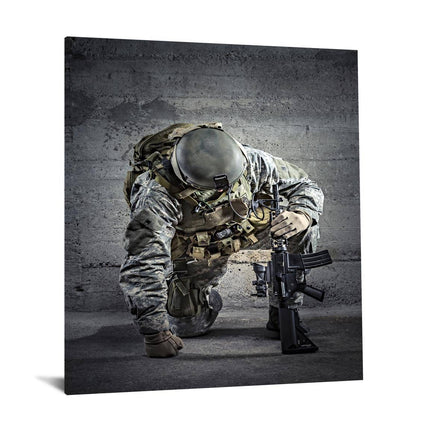 The Kneeling Soldier, clad in camouflage gear with a helmet and tactical vest, holds a rifle with both hands while kneeling against a textured concrete wall—perfect as museum-quality artwork for any home or office.