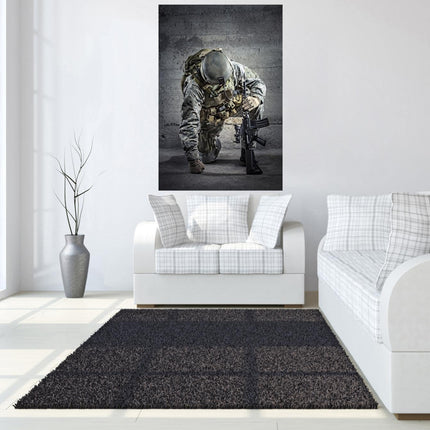 A minimalist living room features a white sofa with plaid cushions. The wall displays the Kneeling Soldier, a museum-quality photo. Beside the sofa, a tall vase with thin branches rests on a tempered glass stand. A dark gray rug complements the light wood floor.
