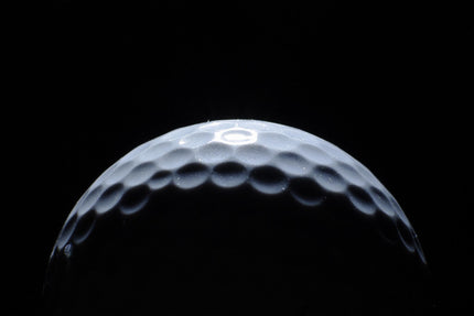 A striking close-up of the Golf Eclipse ball, its dimpled surface dramatically illuminated against a black background, evokes museum-quality art, creating a stark contrast and highlighting the balls intricate texture.