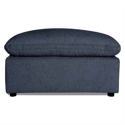 The My Cloud 40 Ottoman features dark gray upholstery with a soft cushioned top and short black legs. Its textured fabric adds to the modern, minimalist design, making it an ideal customizable piece for any living room.