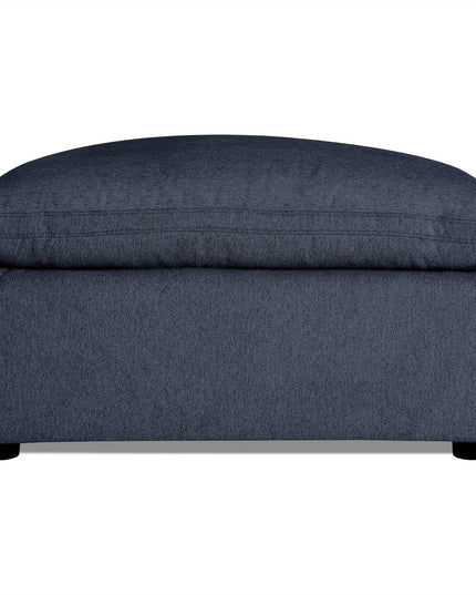 The My Cloud 40 Ottoman features dark gray upholstery with a soft cushioned top and short black legs. Its textured fabric adds to the modern, minimalist design, making it an ideal customizable piece for any living room.