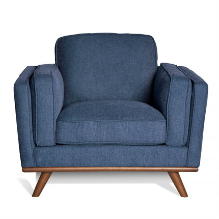 The Maddox Chair is a dark blue mid-century modern armchair featuring plush cushions, wide arms, and angled wooden legs.