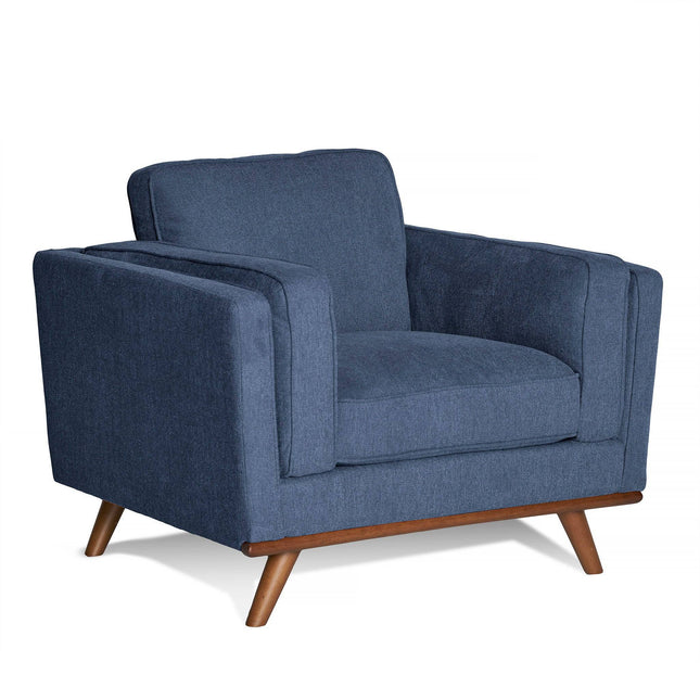 The Maddox Chair is a modern armchair with blue upholstery and wooden legs, featuring a mid-century low, boxy design with plush seat and back cushions. Its sleek style is perfect for any living room or lounge area.