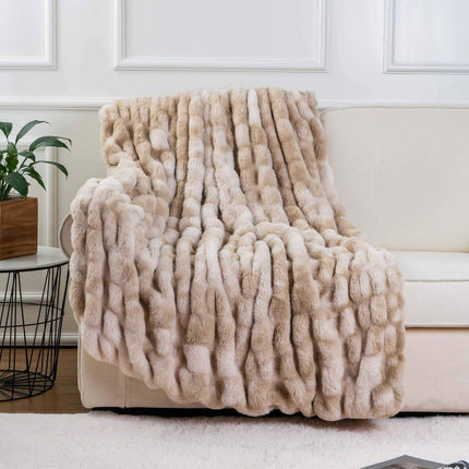 A beige RCL Fur Throw drapes over a light-toned sofa in the living room. A houseplant in a wooden pot rests on a side table beside the sofa, set against a white wall with decorative molding.