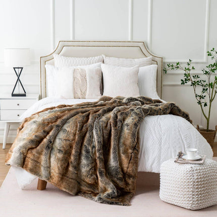 A cozy bedroom showcases a neatly made bed with a white headboard and assorted white pillows. A soft RCL Fur Throw is draped over the bed. Nearby, a white nightstand holds a lamp and green plant, with a tray and teacup on a white pouf.