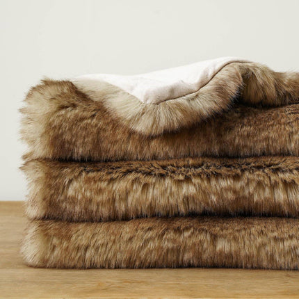 The RCL Fur Throw features a reversible, soft faux fur texture with a realistic brown animal pattern. This luxurious blanket is elegantly displayed on a wooden surface against a light beige backdrop.