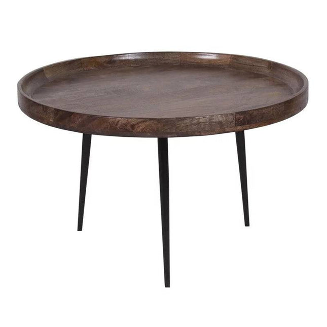 The Mango Bowl Coffee Table is a mid-century style piece crafted from ethically made mango wood, featuring a raised edge and dark finish with support from three slender black metal legs.
