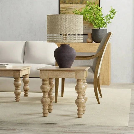 A modern living room boasts a white sofa and wooden coffee table with ornate legs, inspired by French country design. A large dark vase lamp sits on the French Country Side Table, while a sideboard, plant, and chair in the background enhance the rooms neutral tones.