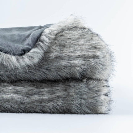 The RCL Fur Throw, a neatly folded gray faux fur blanket with a soft, plush texture and slightly shaggy appearance, creates a luxurious, cozy look. Against the plain white background, its reversible design highlights its inviting texture.