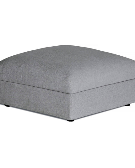 The Lugano Storage Ottoman features a gray square design with a plush cushioned top and smooth fabric. Crafted from premium materials, it has black feet and subtle edge stitching, embodying Italian luxury in a minimalist form.