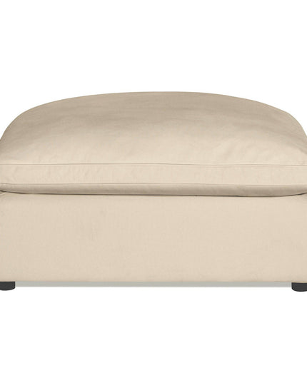 The Peyton Ottoman showcases a minimalist modern style with its beige, rectangular cushion top and simple design. Supported by small dark legs, it provides extra comfort with plush cushioning, making it perfect for any living room or lounge.