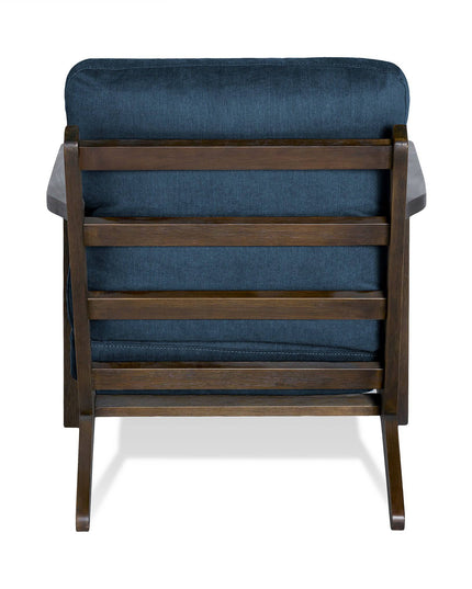 The Peyton Chair features a mid-century design with a plush, dark blue cushioned seat and backrest. The wooden frame showcases horizontal slats and angled legs, combining elegance with coziness.