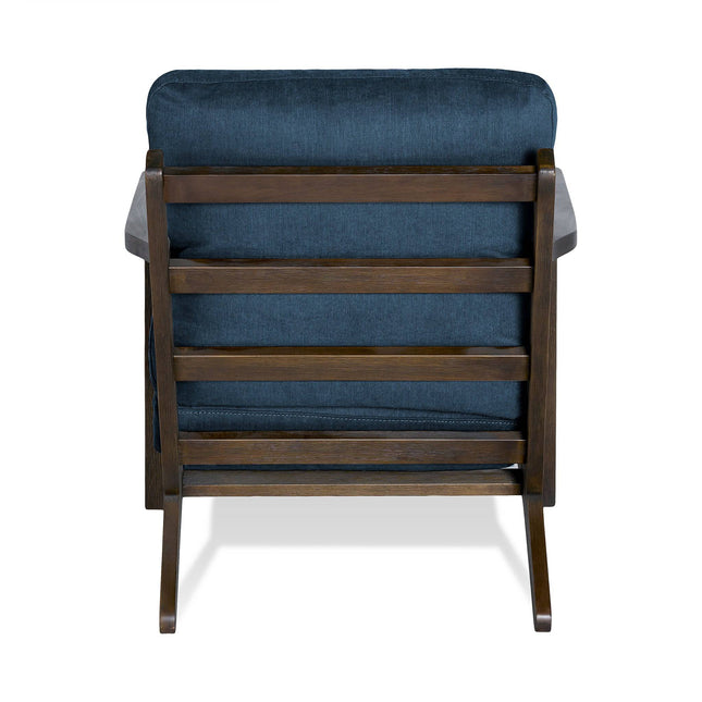 The Peyton Chair features a mid-century design with a plush, dark blue cushioned seat and backrest. The wooden frame showcases horizontal slats and angled legs, combining elegance with coziness.