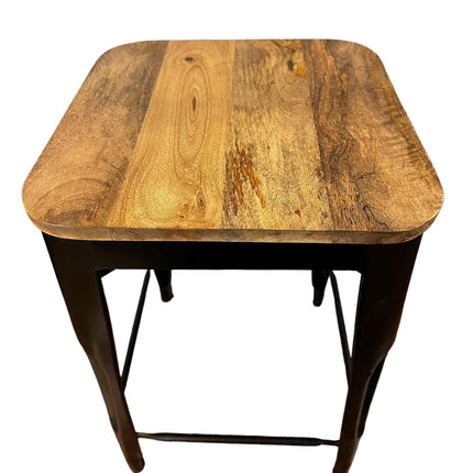 The Mango Counter Stool is a square wooden stool with a mango wood seat featuring varied grain patterns and rounded corners. Its sturdy black metal legs, connected by a bottom crossbar, make it perfect for any kitchen setting as a counter stool.