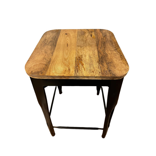 The Mango Counter Stool is a square wooden stool with a mango wood seat featuring varied grain patterns and rounded corners. Its sturdy black metal legs, connected by a bottom crossbar, make it perfect for any kitchen setting as a counter stool.
