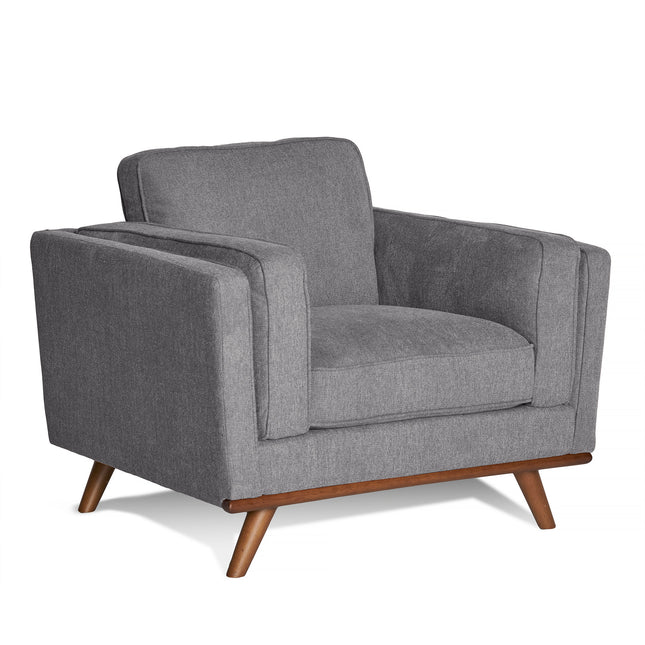 The Maddox Chair is a mid-century modern armchair with plush gray upholstery, wooden legs, and a boxy design. It features thick cushions on the seat and backrest along with wide armrests.
