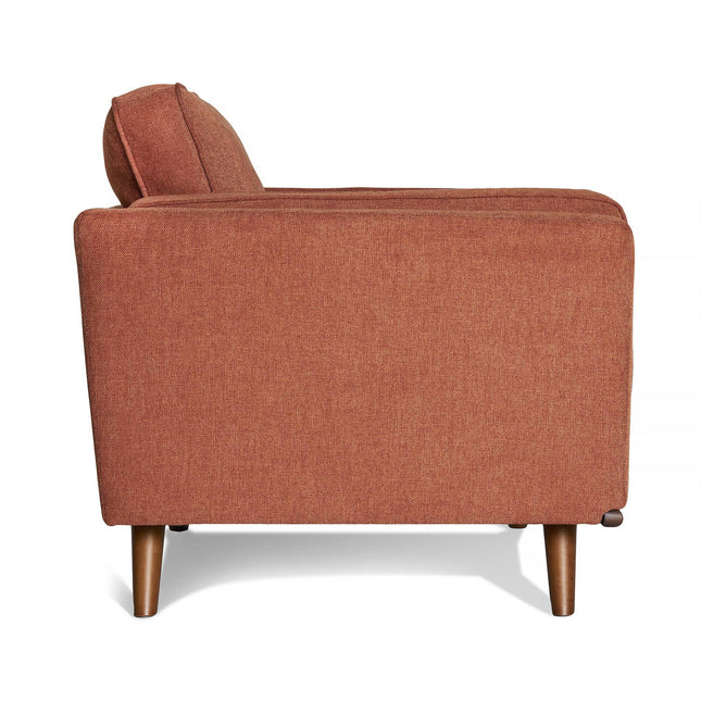 Side view of the Maddox Chair in rust color, featuring mid-century modern design with slightly reclined plush cushions, sleek armrests, and four wooden legs. The texture is soft and inviting.