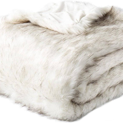 The RCL Fur Throw is a plush, fluffy white reversible faux fur blanket with a textured, soft appearance and subtle greyish streaks, exuding cozy and luxurious allure. Folded neatly, it promises ultimate comfort.