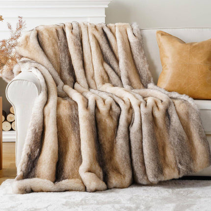 The white sofa sports a fluffy, multicolored RCL Fur Throw that pairs perfectly with the tan leather pillow. A white mantle in the backdrop showcases a small plant and stacked firewood, enhancing the cozy ambiance created by these luxurious throws.